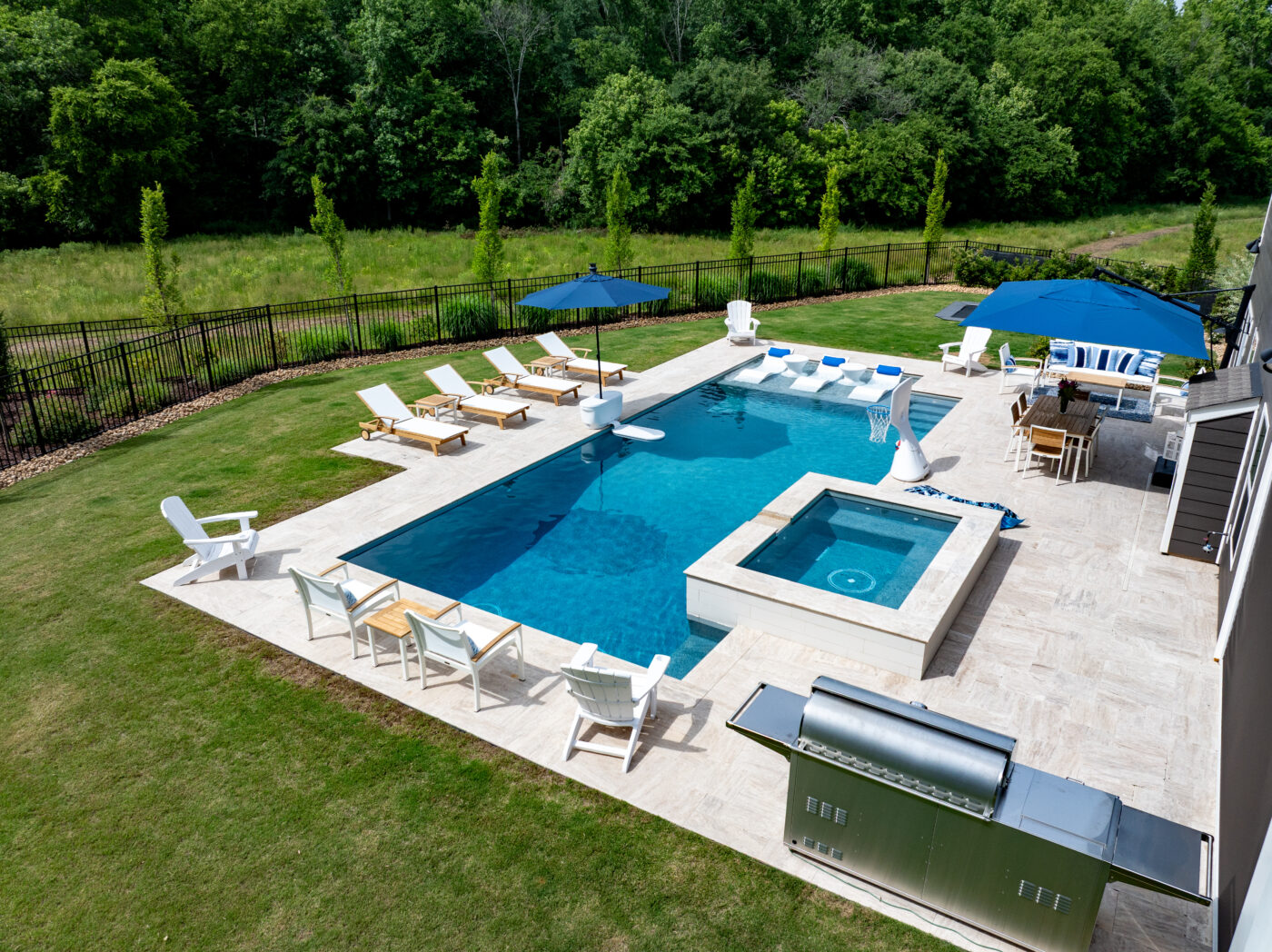 Aerial view of backyard, inground pool surrounded by white, light brown, and blue outdoor furniture
